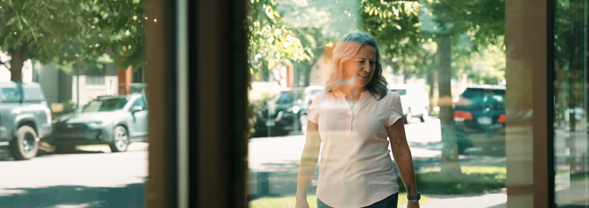 A female breast cancer survivor is walking outside. The picture is taken behind a window showing her healthy and smiling following a breast cancer diagnosis and mastectomy.